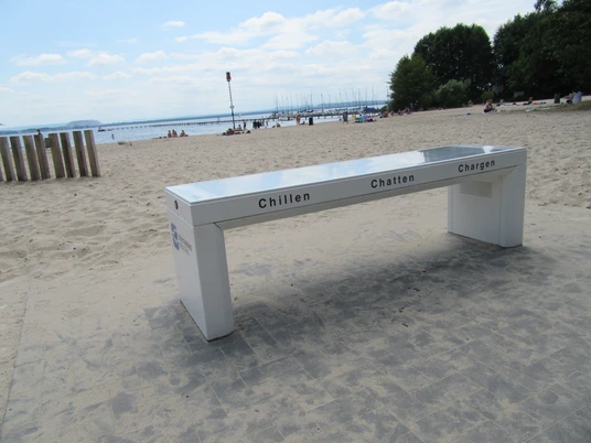 Ladebank am Badestrand Weiße Düne mit Blick auf das Meer, leicht bewölkter Himmel im Hintergrund.