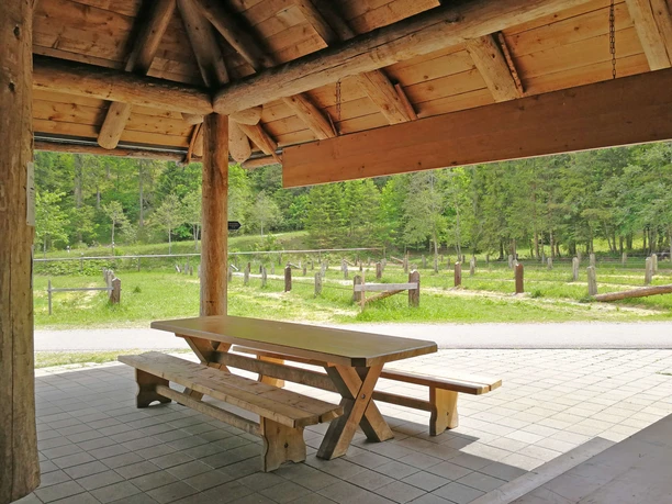 A covered, semi-open wooden hut with a table and benches