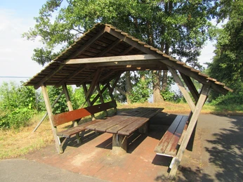 Picknickplatz in der Schutzhütte am Hagenburger Kanal Bastion 2 Holzüberdachte Sitzgelegenheit mit robustem Tisch am Waldrand, vor Blick auf grüne Landschaft.