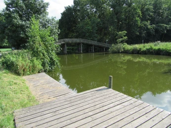 Picknickplatz mit Blick auf die Brücke Hagenburger Kanal vor dem Schloß Ein Picknickplatz mit Holzsteg am ruhigen Kanal, im Hintergrund eine hölzerne Brücke und grüne Bäume.