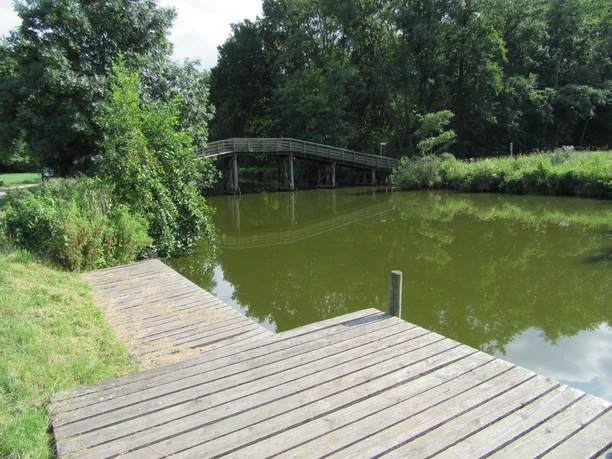 Picknickplatz mit Blick auf die Brücke Hagenburger Kanal vor dem Schloß Ein Picknickplatz mit Holzsteg am ruhigen Kanal, im Hintergrund eine hölzerne Brücke und grüne Bäume.