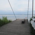 Picknickplatz Sehbrücke Mardorf Holzsteg am Wasser mit ruhiger Seelandschaft, umgeben von Schilf und leicht bewölktem Himmel.