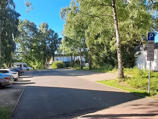 Ein ruhiger Parkplatz umgeben von hohen Bäumen an einer klaren, sonnigen Himmelstag.