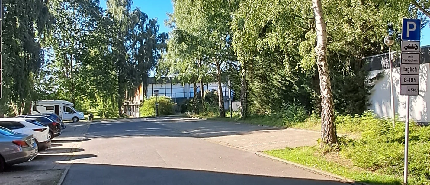 Parkplatz Meerstraße Ein ruhiger Parkplatz umgeben von hohen Bäumen an einer klaren, sonnigen Himmelstag.