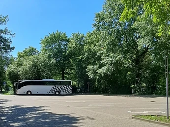 Busparkplatz Bruchdamm Busparkplatz am Bruchdamm mit geparktem weißen Reisebus, umgeben von grünen Bäumen an einem sonnigen Tag.