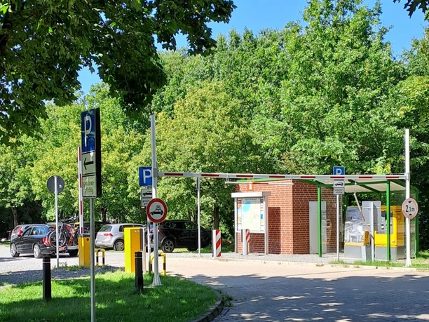 Kassenautomat am Parkplatz Bruchdamm, umgeben von Bäumen und parkenden Autos bei sonnigem Wetter.