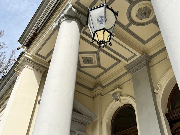 Portikus am Palais Rastede mit Säulen, Hängelaterne und verziertem Eingangsbereich.