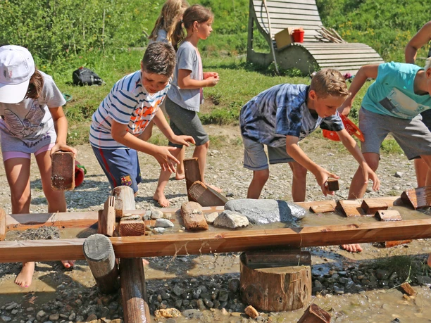 Les enfants utilisent des pierres et des éléments en bois pour retenir l'eau dans un seau en bois.