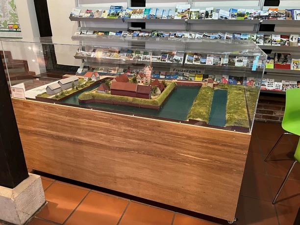 Ein detailreiches Schlossmodell, geschützt von einer Plexiglasvitrine, steht in einem Informationszentrum.