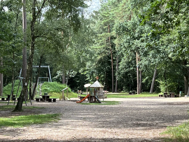 Waldspielplatz Kirchlinteln Ein weitläufiger Waldspielplatz mit Klettergerüst, Rutsche und Schaukeln, umgeben von hohen Bäumen.