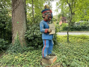 Röbenmarktmann Eine bunte Holzfigur zeigt einen Mann in traditioneller Kleidung, der mit offenen Mund singt.