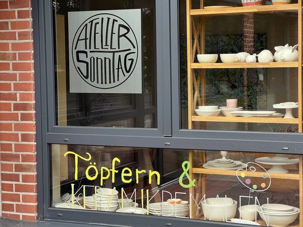 Große Schaufenster einer Töpferei mit Regalen voller Keramik, Schild "Atelier Sonntag".