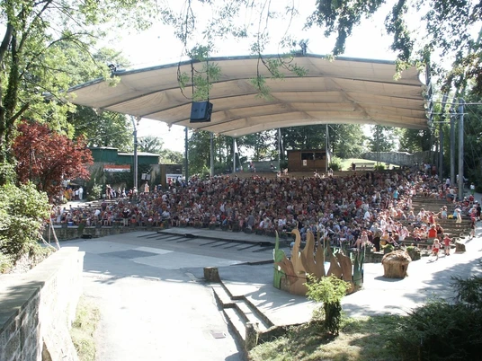 Freilichtbühne Tecklenburg Überdachte Freilichtbühne mit dicht besetzten Rängen, umgeben von Bäumen in parkartiger Umgebung.