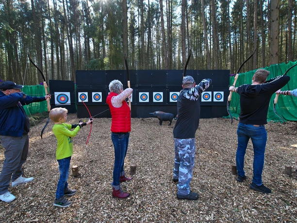 Bogenschießen Gruppe von Menschen beim Bogenschießen im Wald, mit Bögen auf Zielscheiben ausgerichtet.