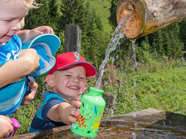 Kind füllt am Brunnen seine Trinkflasche mit Wasser auf
