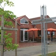 Evangelisch-Freikirchliche Gemeinde Jennelt Backsteingebäude mit großem Metallkreuz und Sitzbereich mit orangefarbenen Sonnenschirmen.