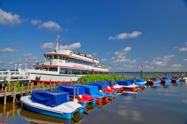 boote-weisse-flotte Ein weißes Ausflugsschiff der Weißen Flotte liegt am Steg, umgeben von farbenfrohen Freizeitbooten.