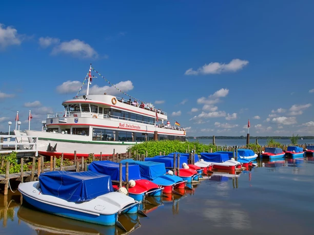 boote-weisse-flotte Ein weißes Ausflugsschiff der Weißen Flotte liegt am Steg, umgeben von farbenfrohen Freizeitbooten.