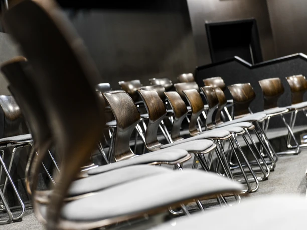 Burgtheater im Institut für Theaterpädagogik der HS Osnabrück Reihen moderner Holzstühle in einem kleinen Theatersaal mit gedämpfter Beleuchtung.