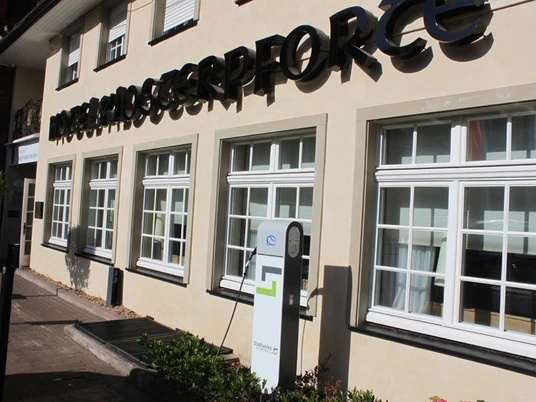 Kfz-Ladestation am Klosterhof Elektrische Ladestation vor einem beige gestrichenen Bürogebäude mit schwarzen Schriftzügen und Fenstern.