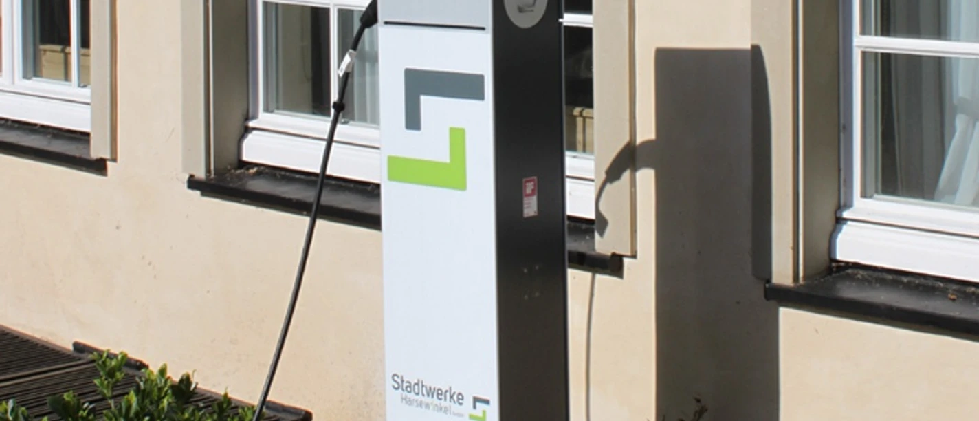 Ladestation für Elektrofahrzeuge vor einem Gebäude mit weißen Sprossenfenstern und umgebenden Pflanzen.