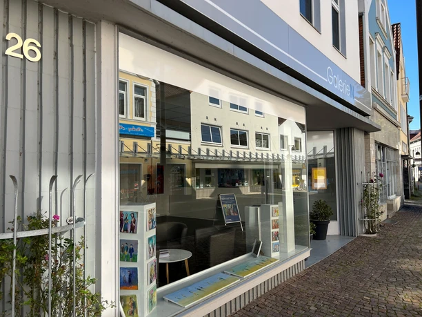 Kunstgalerie mit heller Schaufensterfront, hinter der ein gemütlicher Sitzbereich zu sehen ist.
