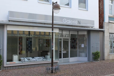 Galerie N Die Galerie N präsentiert eine moderne Glasfassade mit großen Fenstern und einer neutralen Beschilderung.