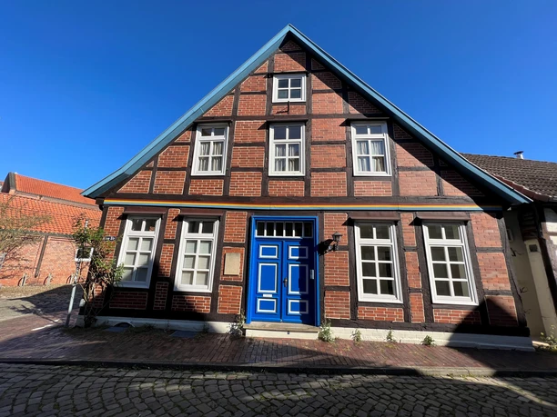 A historic half-timbered house with a striking blue door and a brick facade under a bright blue sky.