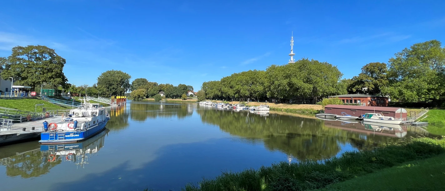 Hafen Nienburg En rolig flodmunding med fortøjede både og omkringliggende frodigt grønt under en blå himmel.
