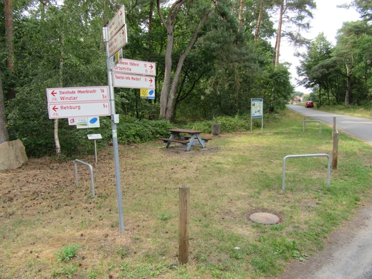 Picknickplatz Poggenecke Ecke am Vogelherd Mardorf Picknickplatz mit Holzbank und Tisch bei Wegweisern, umgeben von Bäumen, neben einer Landstraße.
