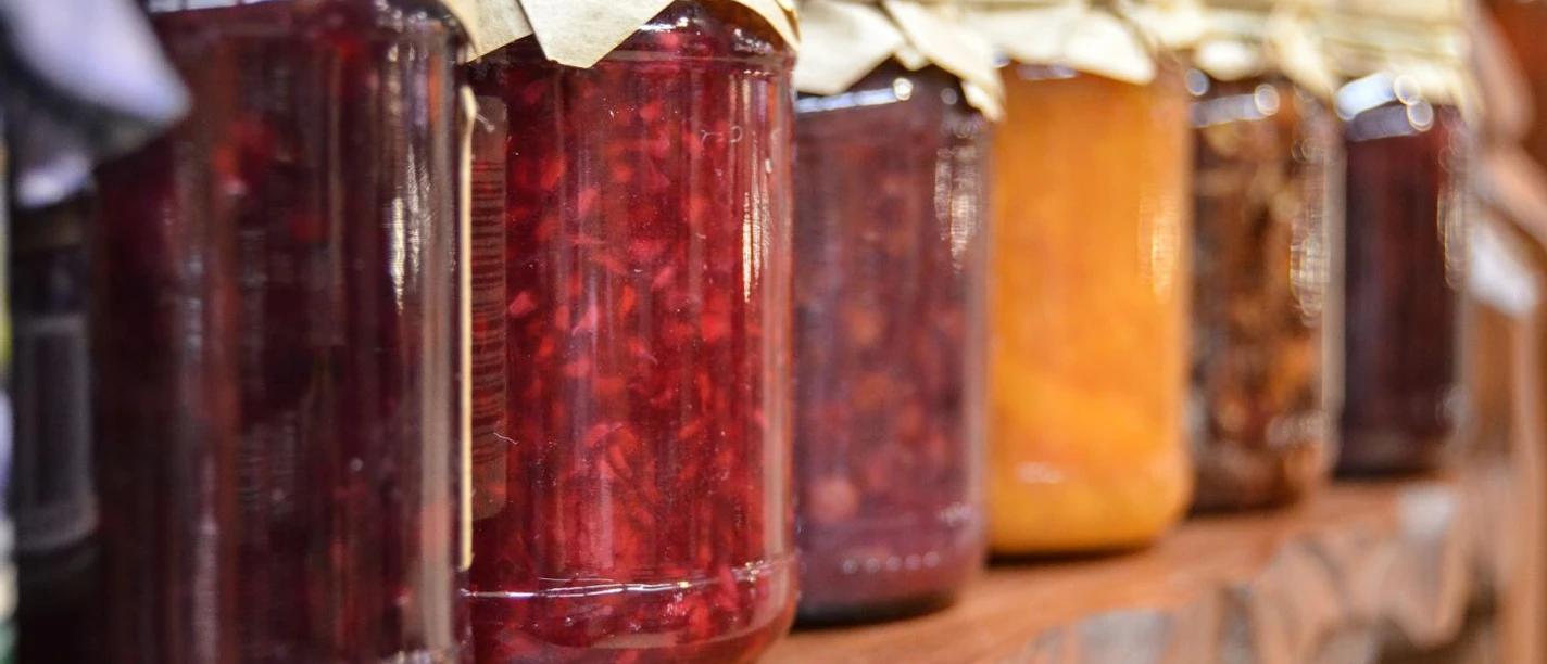 Marmelade (c) Pixabay Verschiedene Marmeladen in Einmachgläsern stehen nebeneinander in einem Regal aus Holz.