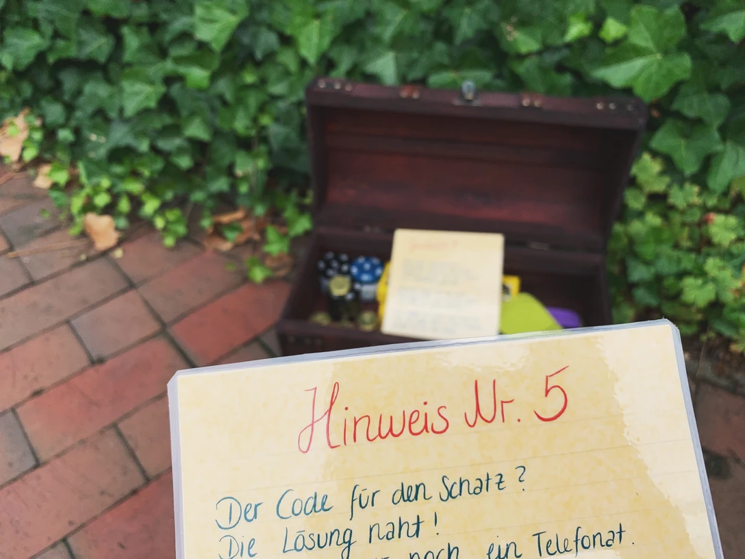 Rätselreise-Wiefelstede-Titelbild Im Vordergrund ein Schild mit der Aufschrift „Hinweis Nr. 5“, im Hintergrund eine geöffnete Schatztruhe.