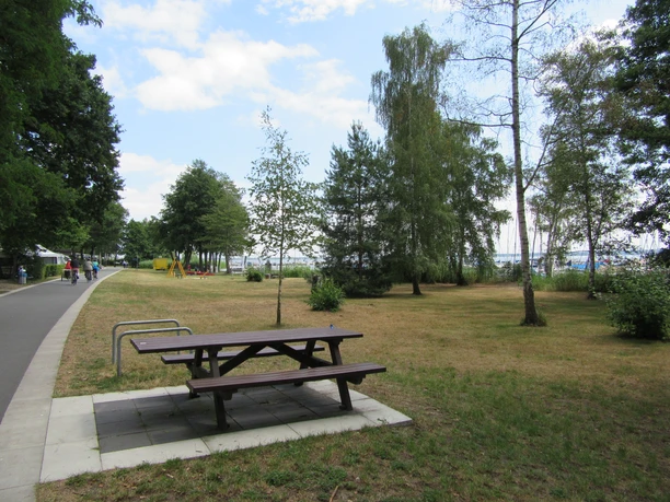 Picknickplatz Uferweg Ecke Raabeweg Mardorf-raabeweg-1 Picknicktisch am Wegesrand neben einer Wiese mit Bäumen, umgeben von Gehweg und Radfahrern.