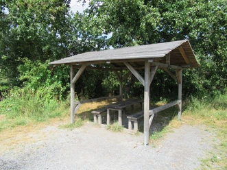 Picknickplatz in der Schutzhütte nähe Aussichtsturm Ostenmeer Ein überdachter Picknickplatz mit Holztischen und Bänken, umgeben von üppigem Grün in einer Waldlichtung.