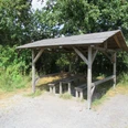 Picknickplatz in der Schutzhütte nähe Aussichtsturm Ostenmeer Ein überdachter Picknickplatz mit Holztischen und Bänken, umgeben von üppigem Grün in einer Waldlichtung.