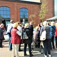 g-stef-hrung-zeitreise-augustfehn-apen Eine Gruppe von Menschen steht vor einem Backsteingebäude und hört einem Redner zu.