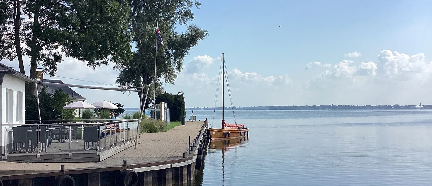 Anleger Insel Wilhelmstein Anleger mit Segelbooten und Bäumen im Hintergrund, an einem ruhigen Gewässer unter blauem Himmel.