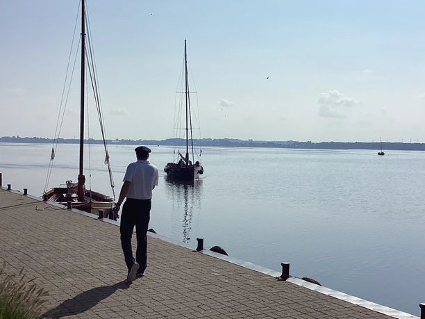 A man walks along the jetty on Wilhelmstein Island while sailing boats float on the water.