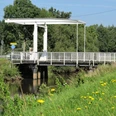 Brücke am Nordloh Kanal Die Brücke am Nordloh Kanal ist eine schlichte, weiße Klappbrücke aus Stahl, die über einen ruhigen, schmalen Kanal im Grünen führt. Sie ist umgeben von einer ländlichen Landschaft mit Gras und vereinzelten Bäumen im Hintergrund.