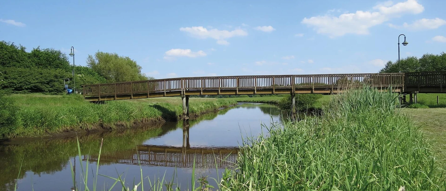 Heeren Wehren Brücke-Apen Die Heeren-Wehren-Brücke in Apen erstreckt sich elegant über einen ruhigen Wasserlauf, umrahmt von saftigem Grün.