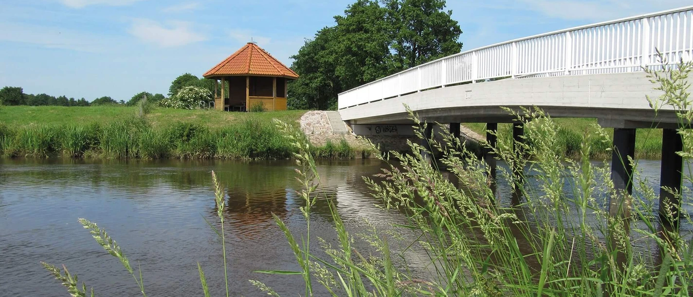 Bokeler Brücke Eine weiße Brücke überspannt das Aper Tief in einer ländlichen Umgebung. Im Hintergrund steht ein Pavillon.