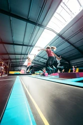 Several people jumping on trampolines arranged in parallel in a bright hall.