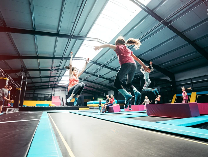 Trampolinpark Abenteuerland Mehrere Personen springen auf parallel angeordneten Trampolinen in einer hellen Halle.Several people jumping on trampolines arranged in parallel in a bright hall.Flere mennesker hopper på trampoliner, der er arrangeret parallelt i en stærkt oplyst hal.Verschillende mensen springen op trampolines die parallel zijn opgesteld in een helder verlichte hal.