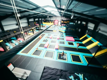 Das Abenteuerland in Bispingen Das Bild zeigt eine große, helle Halle mit verschiedenen Trampolinen in leuchtenden Farben, die zur sportlichen Nutzung angeordnet sind. Bewegung im Hintergrund deutet auf aktive Besucher hin.The picture shows a large, bright hall with various trampolines in bright colors arranged for sports use. Movement in the background indicates active visitors.Billedet viser en stor, lys hal med forskellige trampoliner i stærke farver, der er opstillet til sportslig brug. Bevægelse i baggrunden indikerer aktive besøgende.De foto toont een grote, lichte hal met verschillende trampolines in felle kleuren, opgesteld voor sportief gebruik. Beweging op de achtergrond duidt op actieve bezoekers.