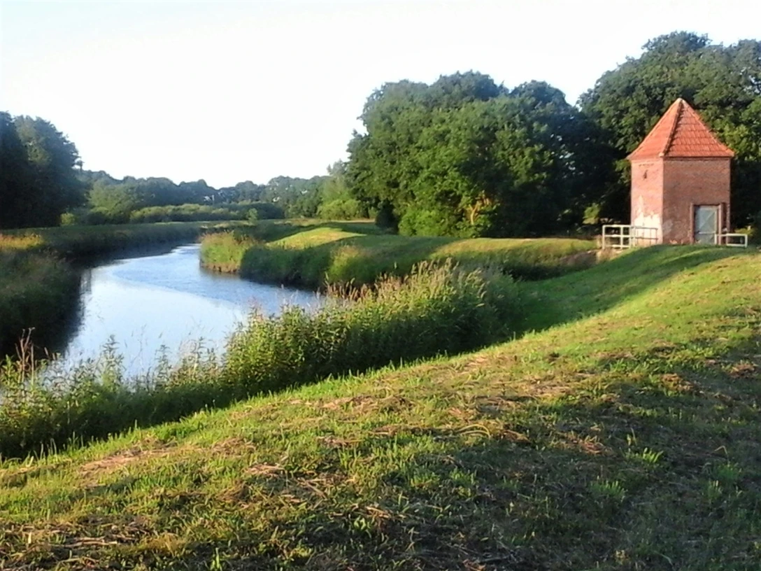 Einfluss Ollenbäke in die Große Süderbäke Der malerische Einfluss der Ollenbäke in die Große Süderbäke bietet einen ruhigen Anblick. Das Wasser, die umliegenden Pflanzen und ein einzeln stehendes Haus schaffen eine harmonische Szenerie.