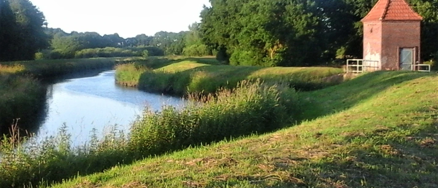 Einfluss Ollenbäke in die Große Süderbäke Der malerische Einfluss der Ollenbäke in die Große Süderbäke bietet einen ruhigen Anblick. Das Wasser, die umliegenden Pflanzen und ein einzeln stehendes Haus schaffen eine harmonische Szenerie.