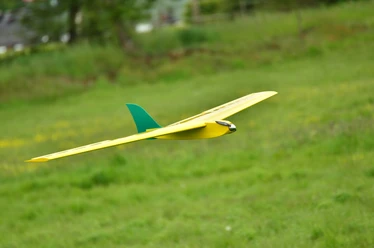 Modellflugzeug im Landeanflug Gelbes Modellflugzeug mit grünem Leitwerk fliegt knapp über einer grünen Wiese im Landeanflug.