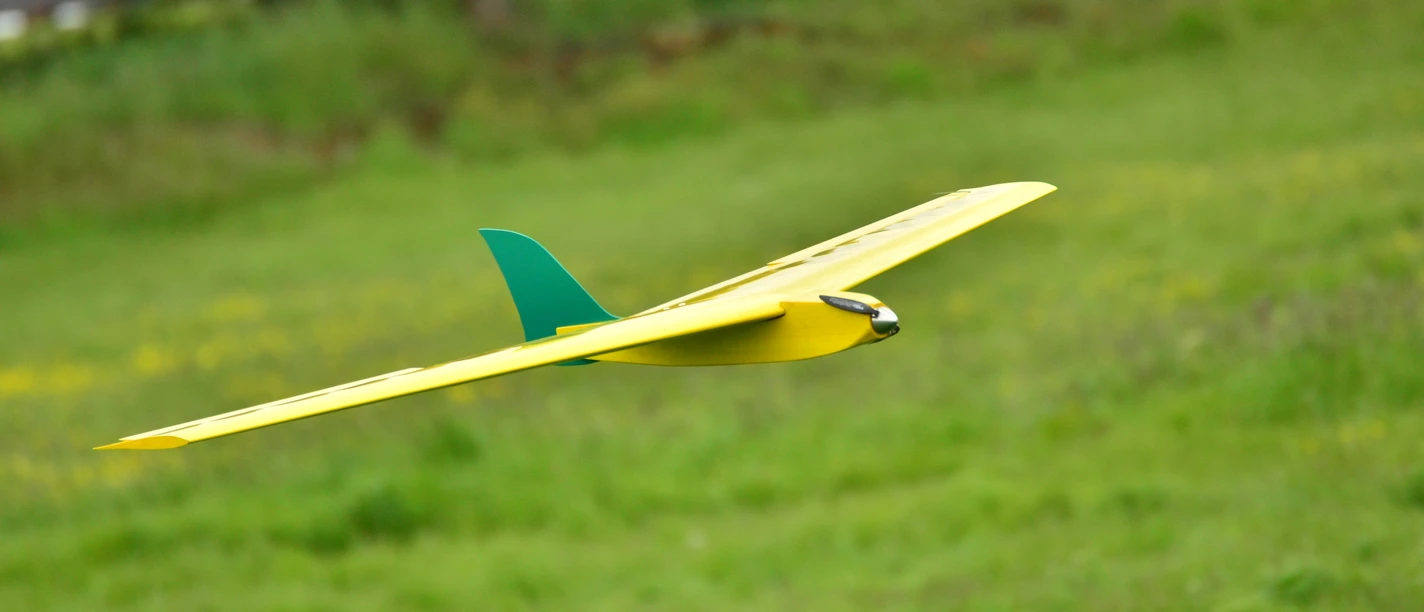 Modellflugzeug im Landeanflug Gelbes Modellflugzeug mit grünem Leitwerk fliegt knapp über einer grünen Wiese im Landeanflug.