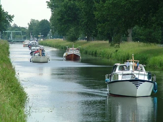 Haren-Rütenbrock-Kanal Mehrere Motorboote fahren auf einem von Bäumen gesäumten Kanal bei ruhigem Wasser.