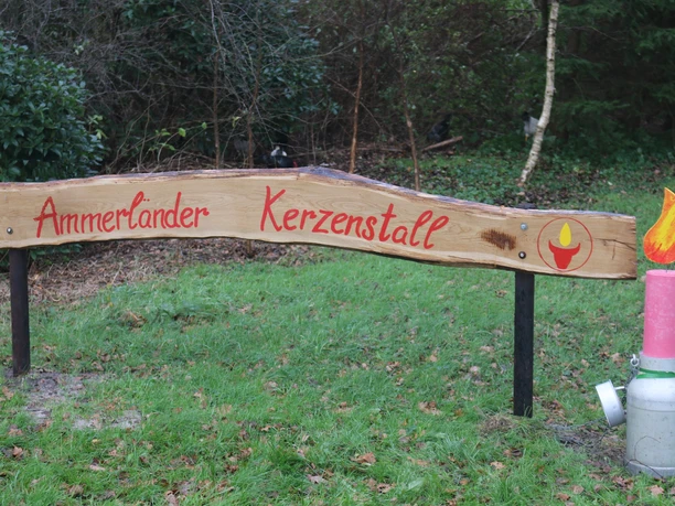 Eingangsschild zum Ammerländer Kerzenstall Holzschild mit roter Schrift Ammerländer Kerzenstall und Kerzendeko auf einer Milchkanne.